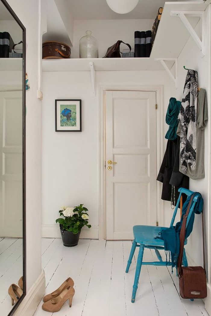 deco couloir avec grand miroir rectangulaire au cadre noir, chaise en bois peinte en turquoise, sol recouvert de bois peint en blanc, pot noir avec plante fleurie en fleurs blanches