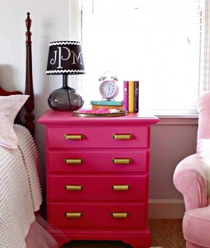 exemple de meuble repeint en rose avec des poignées placard dorées, table de nuit flashy, livres, réveil, lampe de nuit noire, linge de lit rose et blanc