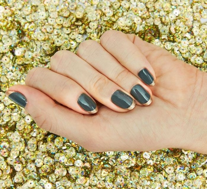 nail art noel facile, vernis à ongles couleur vert de gris avec un bout couleur or, main sur un fond e paillettes dorées
