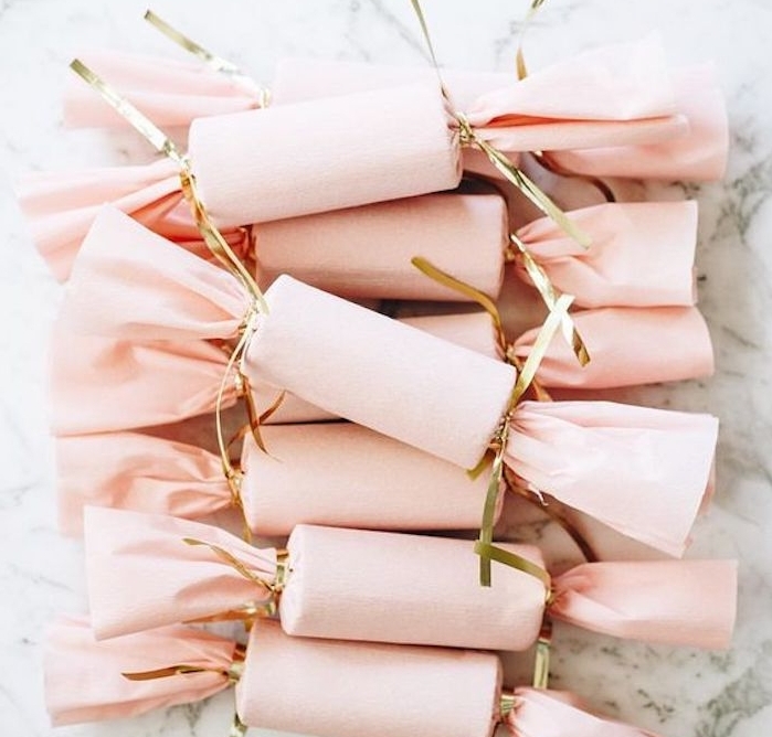 modele de paquet cadeau en papier crépon rose qui emballe une boite en forme de cylindre, façon bonbons, serre dorée