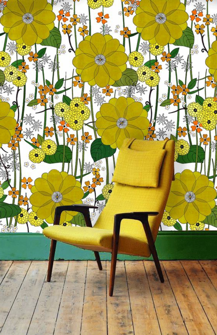 papier peint trompe l'oeil avec des grandes fleurs jaunes, des grandes feuilles vertes, bas du mur peint en vert herbe, parquet bois brut en beige, fauteuil en jaune, moutarde avec des bras en bois marron foncé