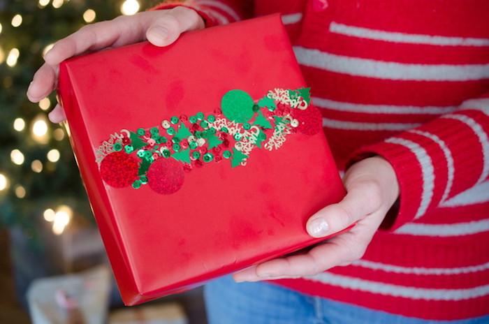 exemple de paquet cadeau noel, résultat final une boite enveloppée de papier roufe et une bande de confettis et paillettes
