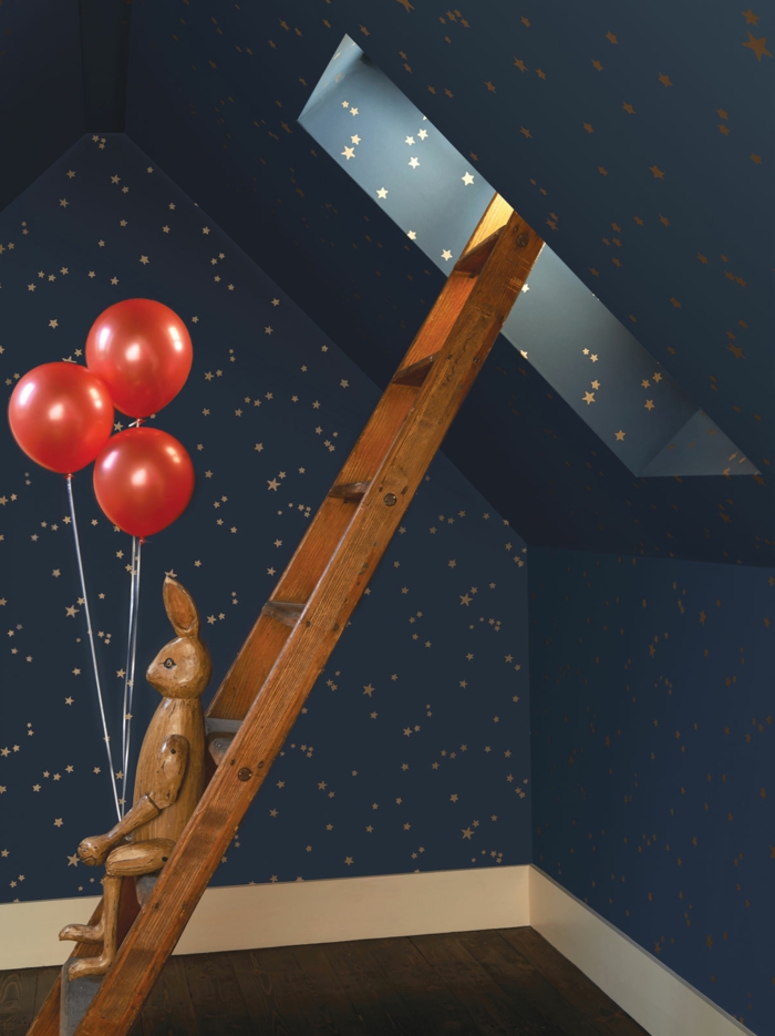 papier peint trompe l'oeil aux motifs ciel étoilé pour une chambre d'enfant sous les combles, avec fenêtre, parquet en marron foncé, escalier en bois clair, lapin en bois avec trois ballons rouges 