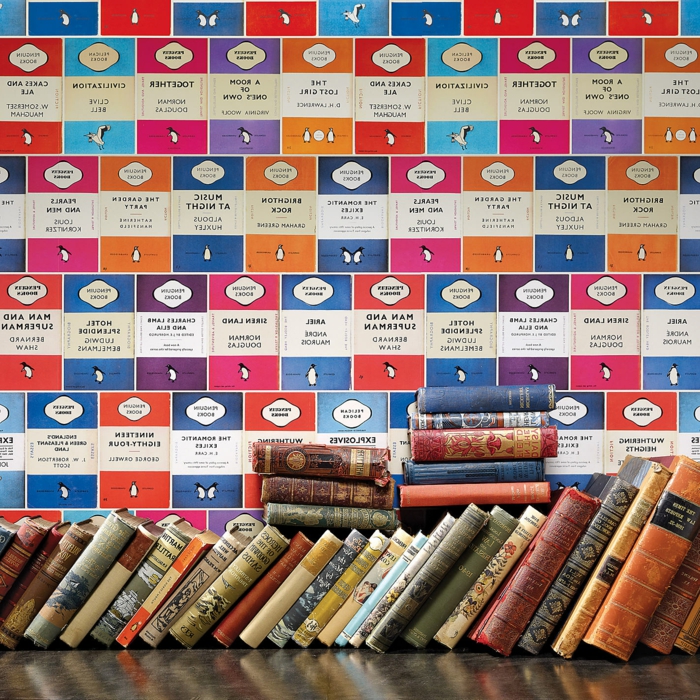 papier peint trompe l'oeil avec des motifs BD en bleu, fuchsia et rouge, murs d'une bibliothèque avec beaucoup de livres, titres anciens, couvertures usées