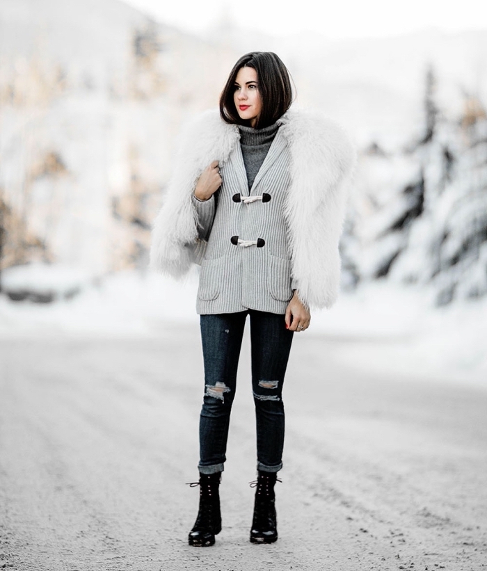 tenue hiver, modèle de jeans foncés déchirés portés avec gilet et pull gris, bottines avec lacets et manteau faux fur blanc