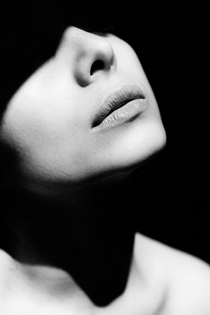 portrait noir et blanc, visage de femme dans la pénombre, avec les lèvres mises en valeur, accent rouge a lèvres, la forme du nez avec une belle forme