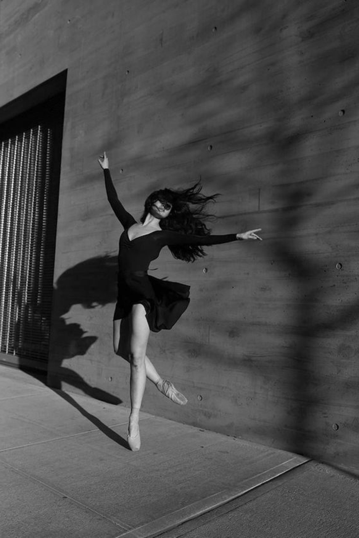 image noir et blanc, femme qui danse, habillé d'une robe noire, avec décolleté en V plongeant, les bras grands ouverts, tels des ailes d'oiseau