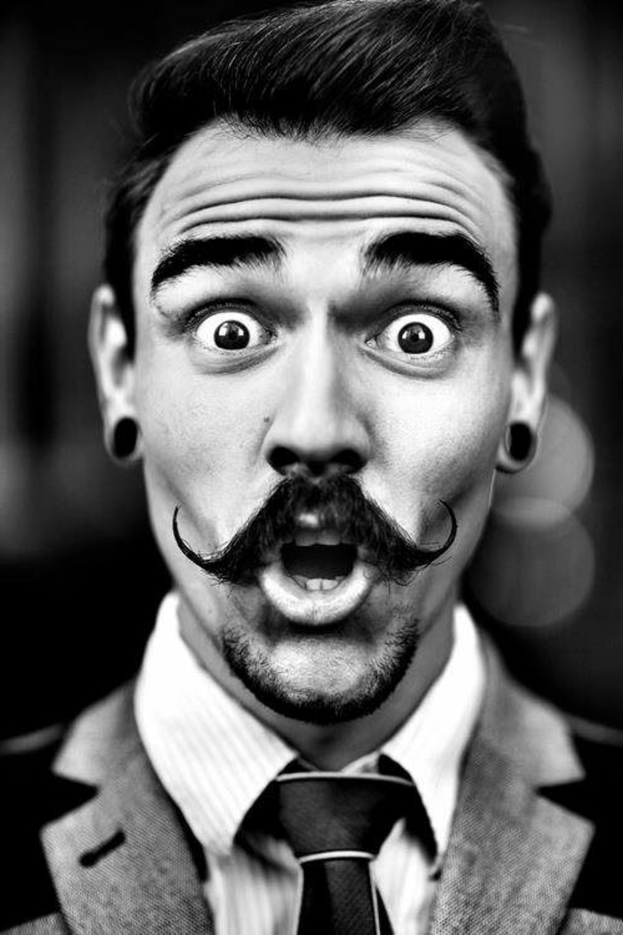 photo noir et blanc, homme avec expression très surprise, cravate noire, bouche grande ouverte, moustache bien soignée avec du gel et de la cire