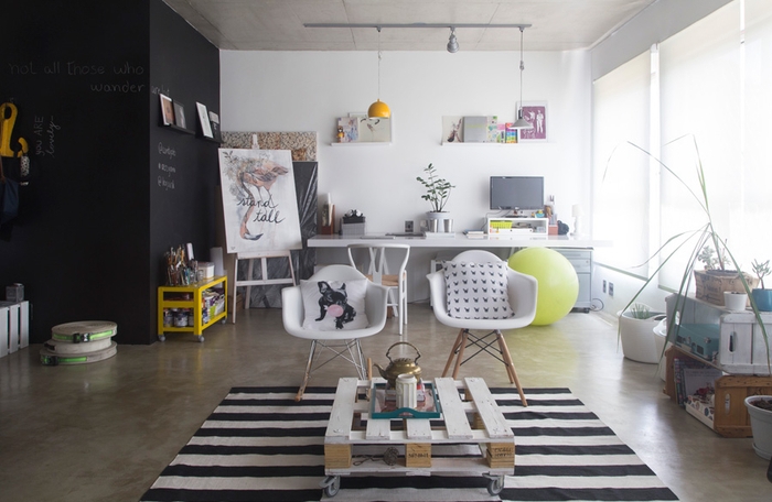 un salon de style loft industriel en noir et blanc avec une table basse en palette assortie avec des chaises scandinaves et un tapis à rayurers
