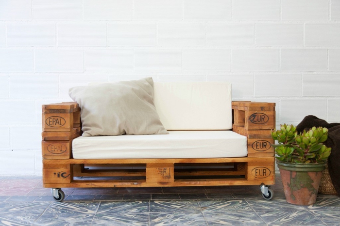 un canapé en palette deux places avec roulettes aux lignes simples avec coussins et matelas pour un maximum de confort