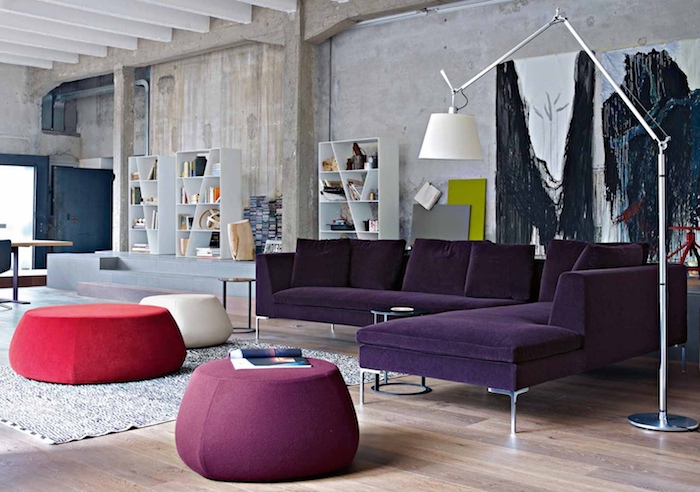 déco loft industriel dans un salon contemporain avec canapé violet, tables basses en mauve, blanc et rouge, tapis rouge, parquet clair, etagere livres, mur usé