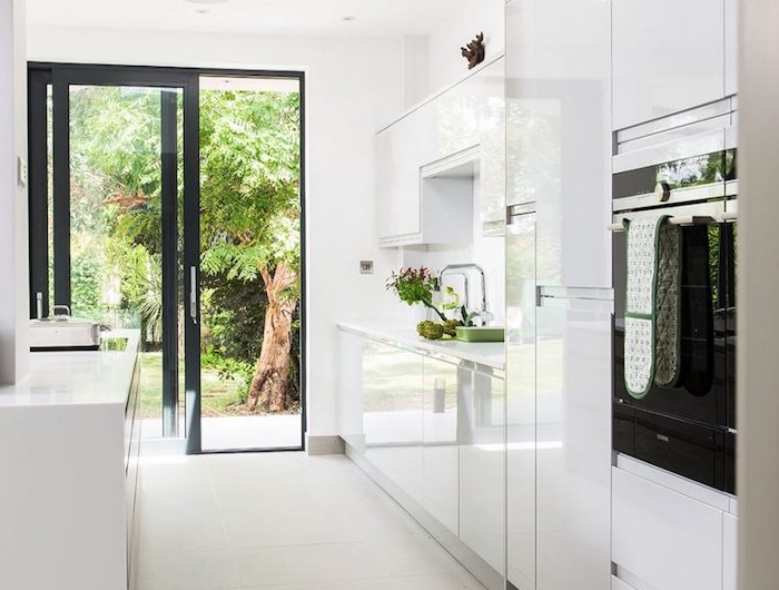 cuisine moderne blanche, meubles cuisine finition brillante laquée, porte vitrée avec encadrement noir, four noir