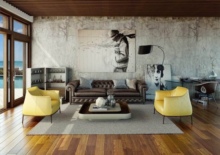 décoration industrielle salon avec canapé en cuir marron foncé, fauteuils jaunes, tapis gris, sol en parquet marron, mur usé, plafond en bois, cadres tableaux graphiques en noir et blanc