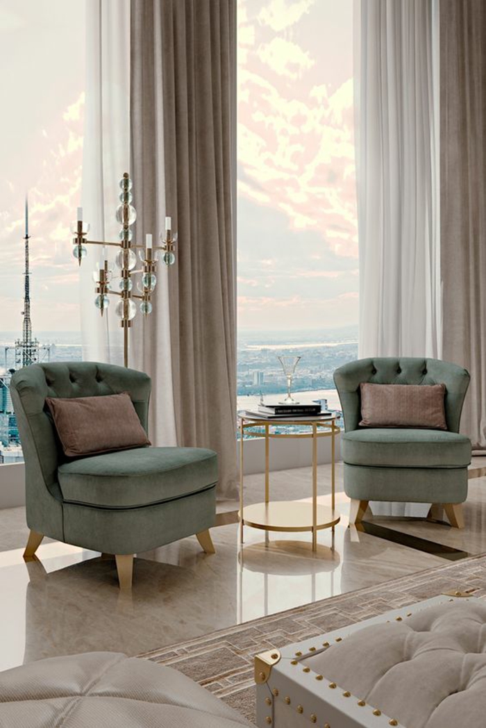 deco salon design avec deux grands fauteuils en vert pistache, sol recouvert de marbre beige lisse et brillant, table ronde avec base haute en métal doré, luminaire sur pied en métal doré avec des boules en verre, rideaux en gris perle