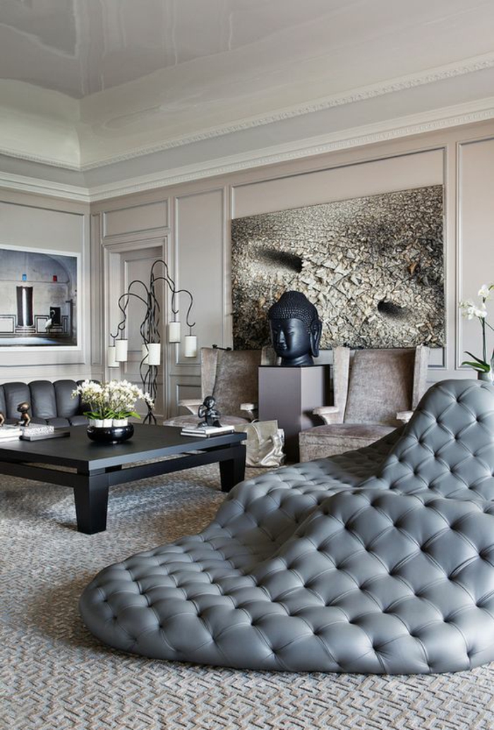 maison moderne de luxe, dormeuse énorme design en gris perle, avec effet matelassé, tableau au mur en blanc et gris. table carrée en noir, murs en beige 