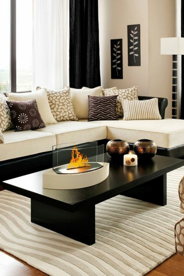 salon moderne de luxe avec canapé en blanc et noir angulaire, table rectangulaire noire en bois laquée, tapis rectangulaire sous la table en blanc et gris clair aux motifs dunes, petite cheminée en forme d'iris sur la table