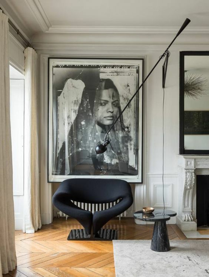 amenagement salon avec parquet en jaune, grande photographie portrait de femme Afghane, style ethno, cheminée blanche, fauteuil design en noir en tissu et base en marbre noir , tapis en noir et blanc