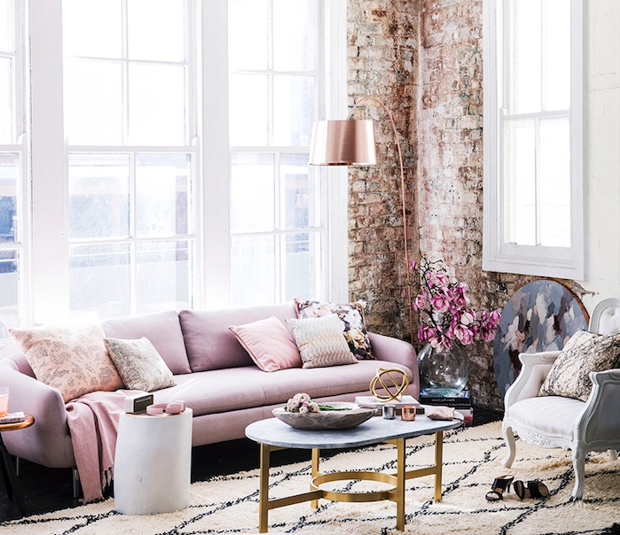 exemple de deco style industriel dans un salon feminin avec canapé rose, table basse marbre et laiton, tapis noir et blanc, mur en briques, luminaire rose gold