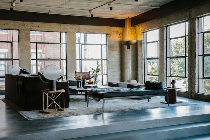 deco stule industriel dans un salon spacieux avec canapé couleur foncée, table basse bois, chaise longue en metal et matelas bleu, murs effet beton