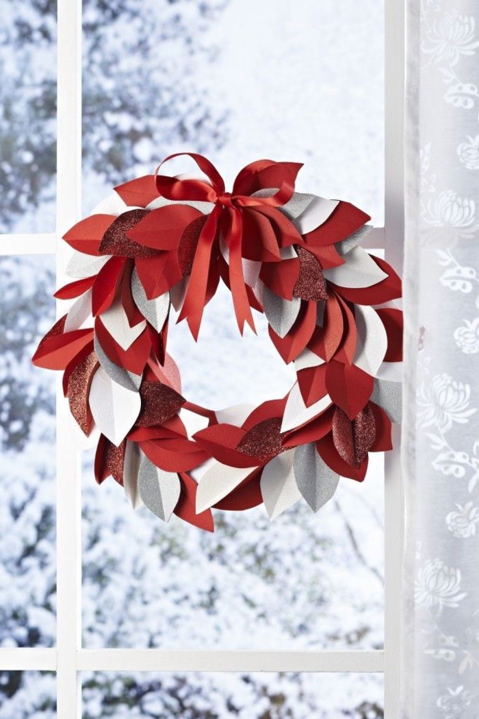 décoration de noel à fabriquer pour adultes, une couronne de noël en blanc et rouge réalisée avec des feuilles en papier, fixée à la fenêtre à l'aide d'un joli noeud satiné
