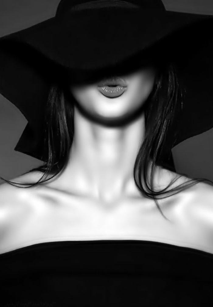 photo noir et blanc, dame avec capeline noire large, rouge à lèvres en couleur corail, robe bustier noire, peau lisse et bien entretenue