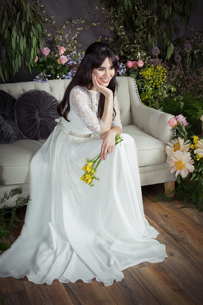 robe de mariée blanche, manches en dentelle, sofa gris clair, bouquet de fleurs jaunes