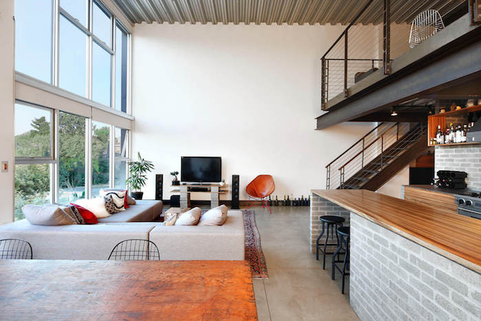 meubles tv industriel en bois et bloc en béton, sol en dalles effet béton, canapé d angle gris, tapis oriental, ouverture sur une cuisine, mezzanine