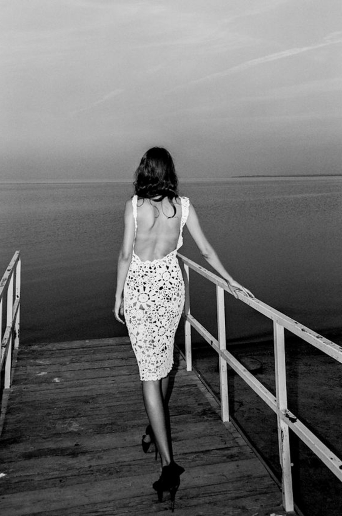 image noir et banc, portrait noir et blanc, femme avec robe en dentelle blanche, effet ajouré, avec des talons aiguilles en noir , marchante sur le quai en face de la mer