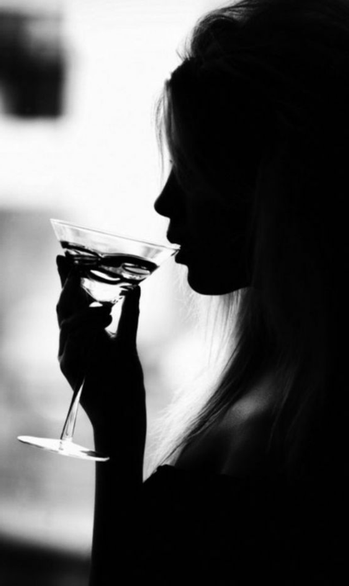 photo femme noir et blanc, femme sexy aux cheveux longs buvant un Martini, silhouette dans la pénombre 