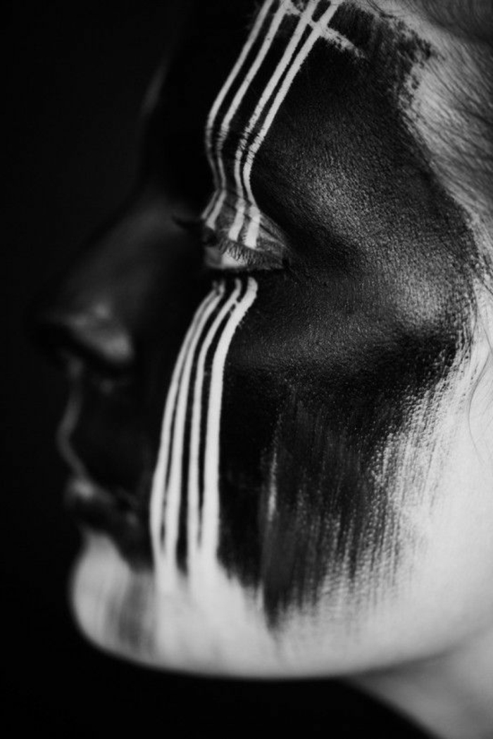 portrait noir et blanc, visage de femme avec des traits de crayon blanc sur une des paupières, visage peint en noir, façon style tribal