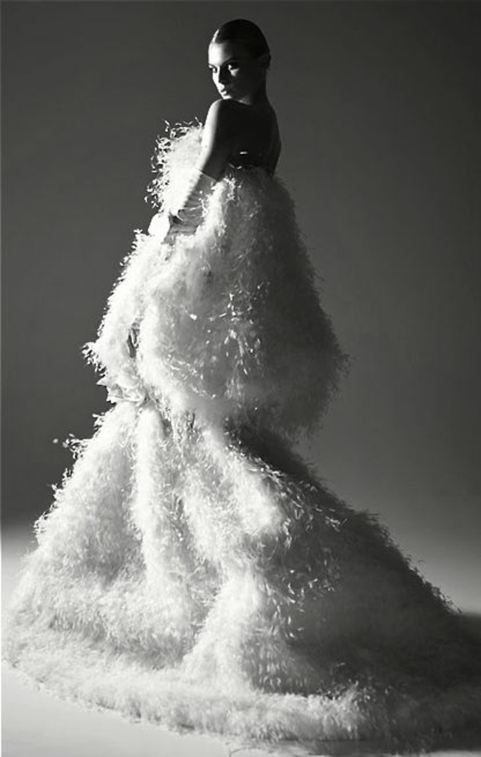 photo femme noir et blanc, avec robe en plumes blanches, femme au dos nu, cheveux en chignon lisse, look de fêtes et de grande soirée 
