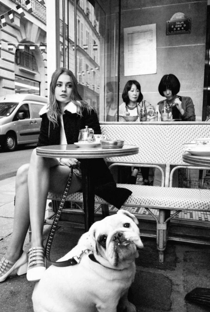 photo femme noir et blanc, jeune femme dans un bistrot avec un chien blanc qui regarde le photographe, femme rêveuse , chic parisien