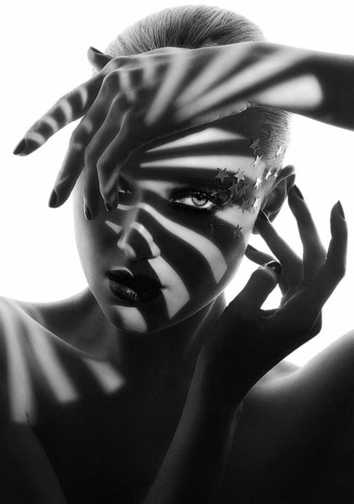portrait noir et blanc, femme qui a mis ses deux paumes près du visage et a obtenu un beau jeu d'ombres, comme des rayons de soleil