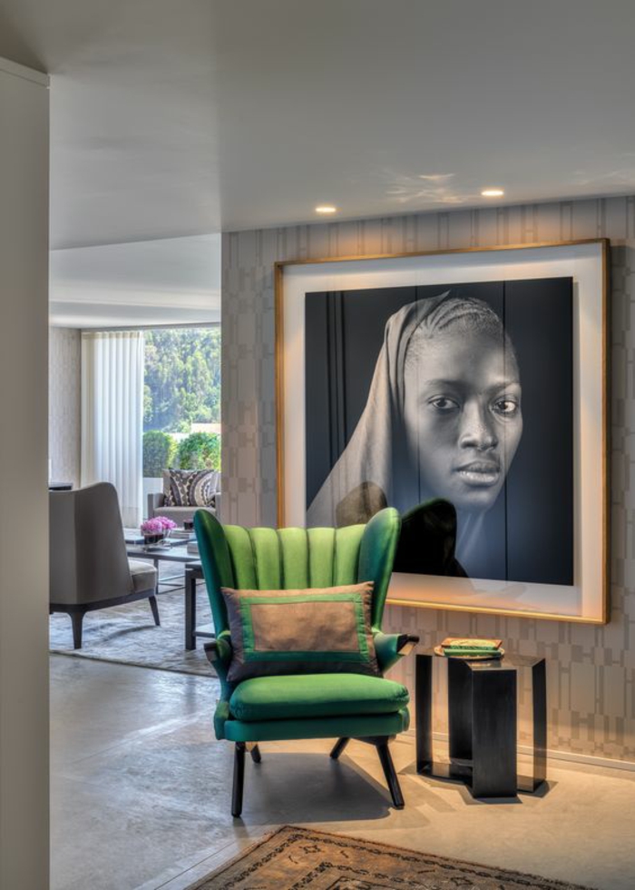 amenagement salon avec grande photographie en noir et blanc au cadre doré, fauteuil en vert avec coussin en vert et marron, table en métal forgé en gris fumé, tapis oriental