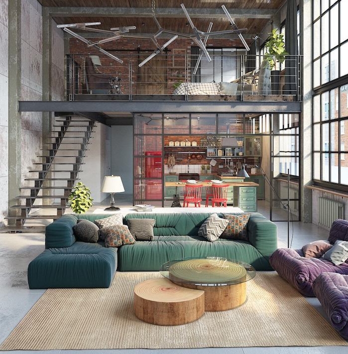 exemple de salon industriel moderne avec canapé vert et bleu, tables basses en tronc de bois, tapis beige, fauteuils mauves, cuisine séparée avec verrière