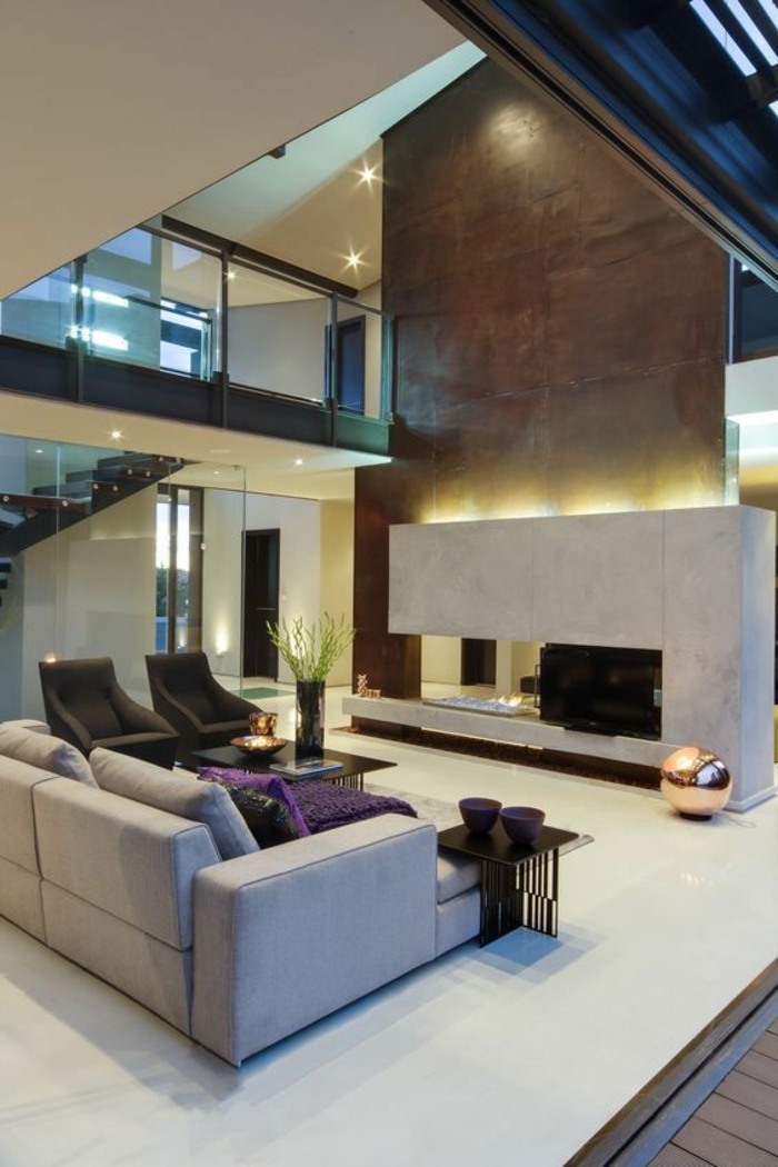maison moderne de luxe, espace très grand, grande cheminée en pierre blanche avec un tube énorme revêtu de bronze pour la sortie des fumées, canapé en gris clair