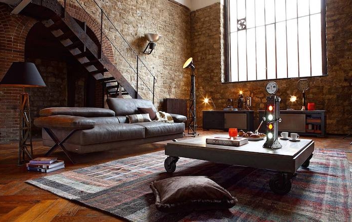 modele de table basse industrielle à roulettes dans un salon avec canapé en cuir gris, tapis à carrés, meuble en métal, coussin marron, mur en briques