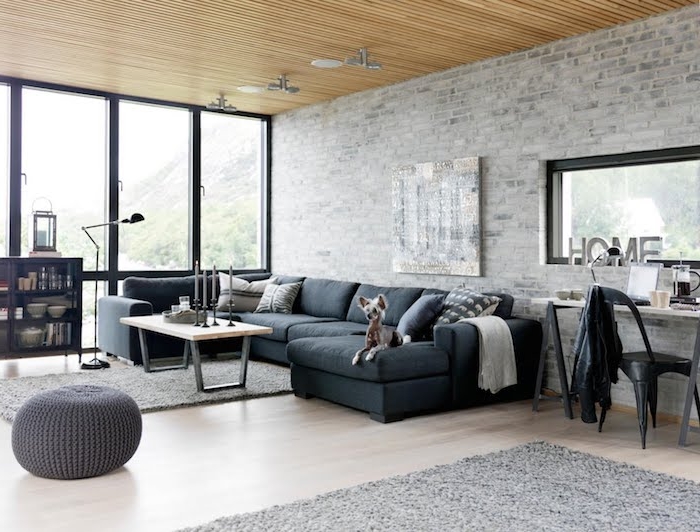 modele de table basse industrielle en bois et metal dans un salon loft avec canapé noir, tapis gris et pouf gris, plafond en bois, mur en briques grisées