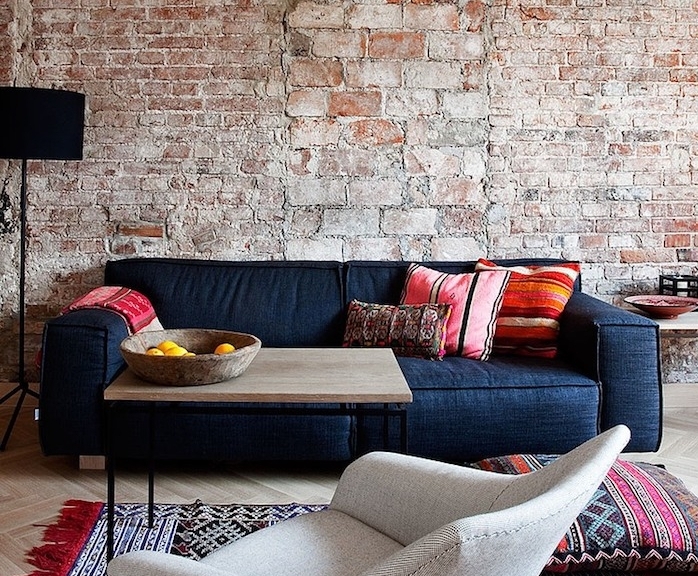 mur en briques dans un salon moderne avec canapé noir, parquet clair, table basse en bois et metal, tapis oriental