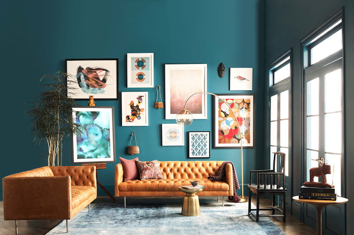 exemple de canapé pas cher, deux canapés en cuir sur un mur de fond en bleu canard, deco murale de cadres artistiques, table basse minimaliste