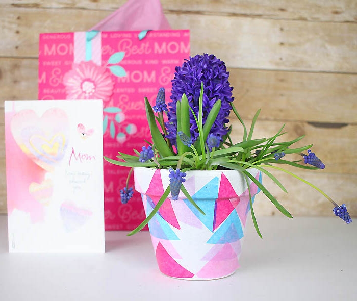 pot de fleur blanc customisé de triangles de papier colorées en bleu, rose et fuchsia, muguet, idée cadeau fête des mères a faire soi meme