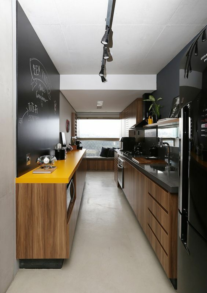cuisine petit espace, cuisine en longueur, meubles n noir et jaune, carrelage blanc, tableau noir pour des notes sur un mur entier 