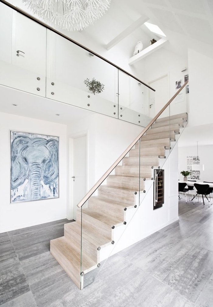 une ambiance de galerie d'art crée par l'habillage escalier en bois naturel, la rambarde en verre, la toile haute et le grand tableau accroché sous l'escalier