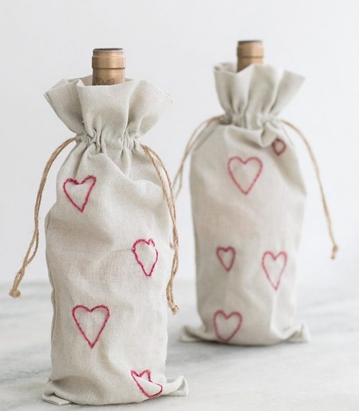 bouteilles de vin dans des petits sacs à bouteille blanc cassé avec motif coeur rouge cousu, cadeau saint valentin pour les amateurs du vin