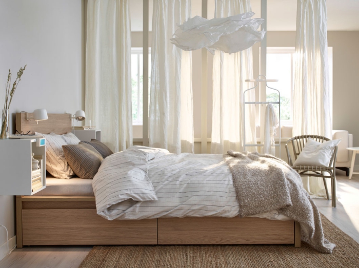 ambiance cozy dans la chambre à coucher adulte avec décoration en voiles longs de nuance écru et meubles en bois clair