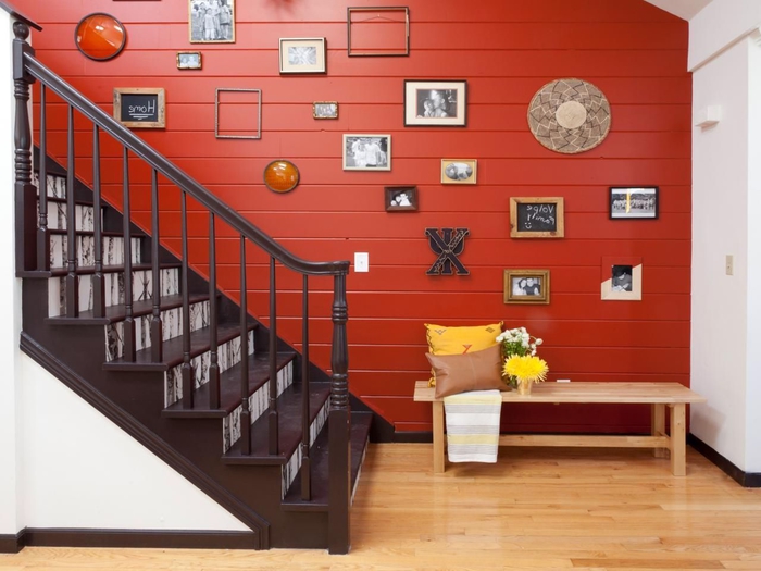 une cage d'escalier aux couleurs contrastées agrémentée d'une galerie murale, lambris rouge tonique qui fait ressortir l'escalier en blanc et marron 