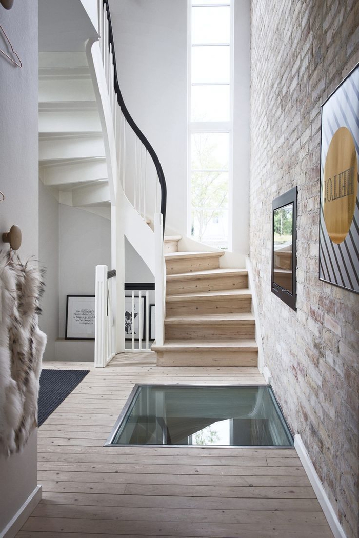 une cage d'escalier de style scandinave baignée de lumière naturelle, des marches en bois naturel et une balustrade peinte en blanc en harmonie avec le plancher en bois