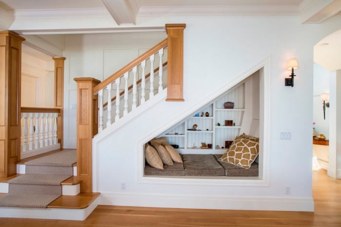 etagere sous pente en bois peint en blanc avec banc et coussins décoratifs pour un coin de lecture sous l'escalier