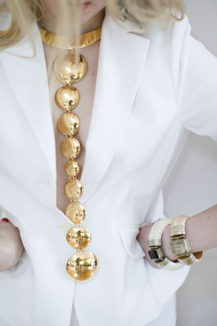 bijou extravagant et long avec des boules en métal couleur or, soirée chic détail choc, bijou porté sur une veste blanche classique
