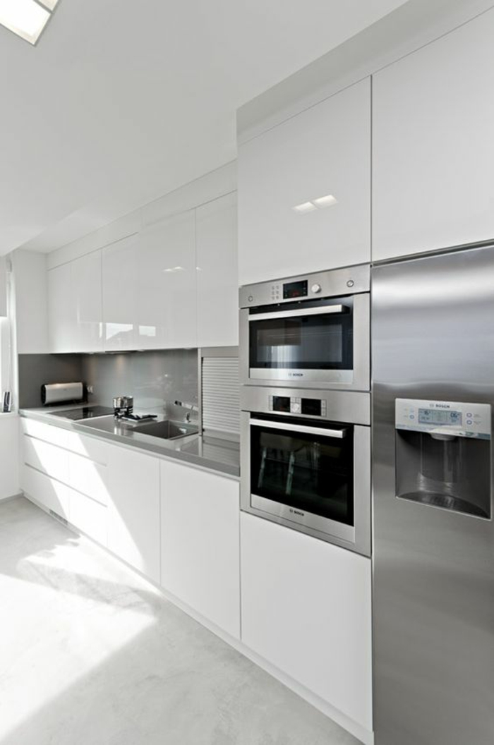 cuisine intégrée, petite cuisine équipée, meubles blancs et électroménagers en métal couleur argent, sol avec des dalles carrelage blanc-gris 